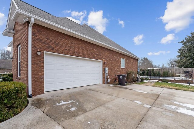 view of side of home with roof with shingles, brick siding, driveway, and fence