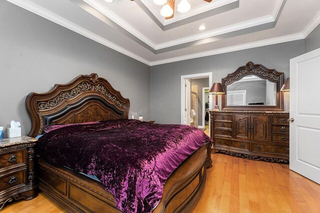 bedroom with a raised ceiling, ensuite bath, ceiling fan, ornamental molding, and light wood-style floors