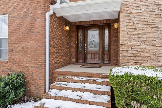 snow covered property entrance featuring stone siding and brick siding