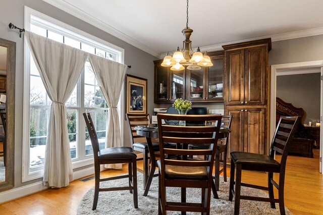 dining area featuring crown molding, plenty of natural light, an inviting chandelier, and light wood-style floors