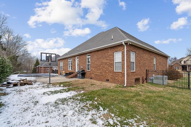 view of snowy exterior with a yard, brick siding, crawl space, and fence