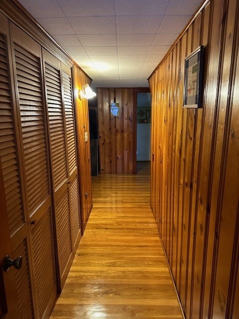 hallway featuring light wood-type flooring and wooden walls