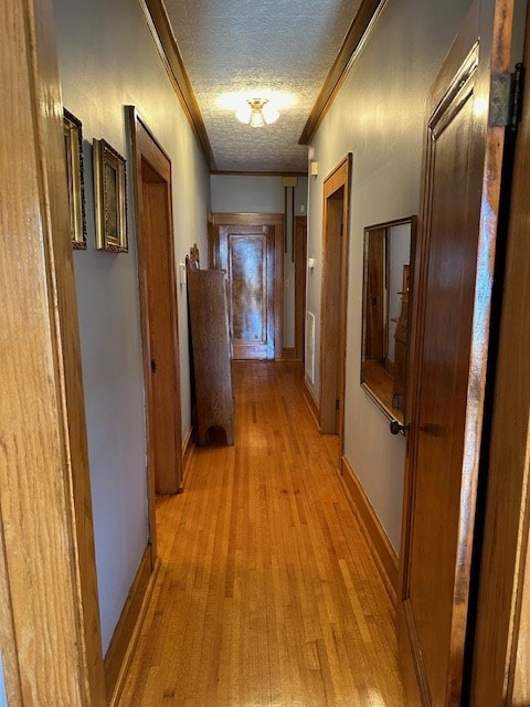 corridor featuring a textured ceiling, ornamental molding, light wood-type flooring, and baseboards