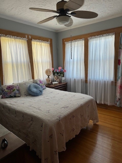 bedroom with a textured ceiling, multiple windows, wood finished floors, and a ceiling fan