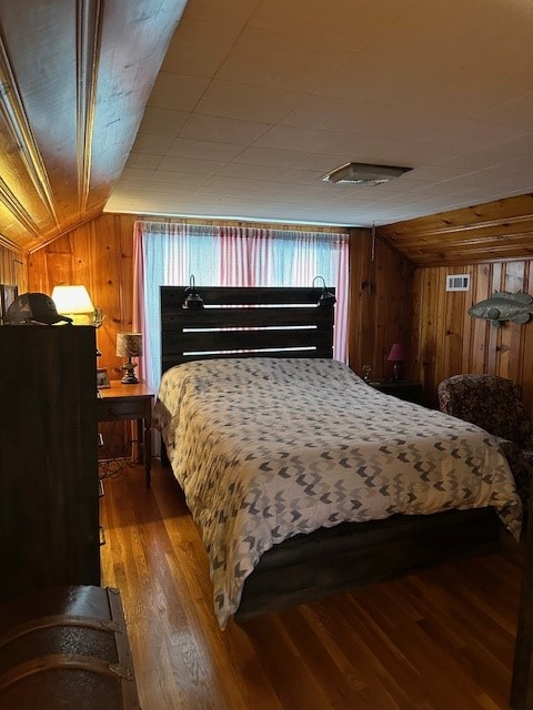 bedroom with lofted ceiling, wood walls, and wood finished floors