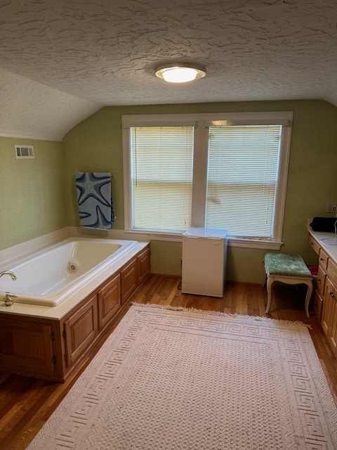 full bathroom with visible vents, wood finished floors, a garden tub, vaulted ceiling, and a textured ceiling