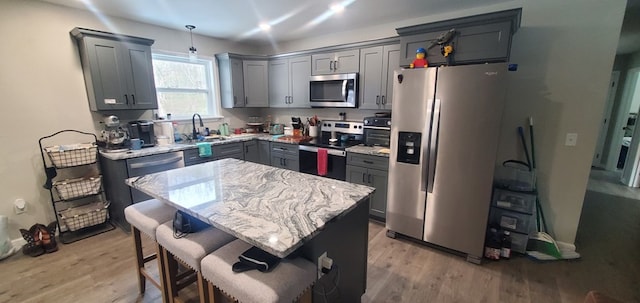 kitchen with light wood finished floors, gray cabinets, hanging light fixtures, appliances with stainless steel finishes, and a kitchen island