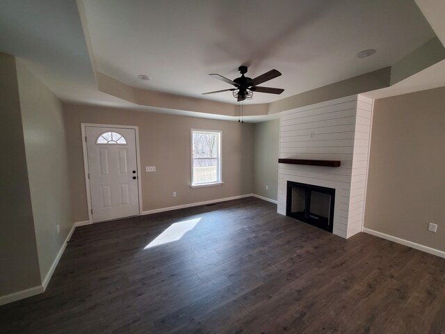 unfurnished living room featuring dark wood-style flooring, a fireplace, a raised ceiling, ceiling fan, and baseboards