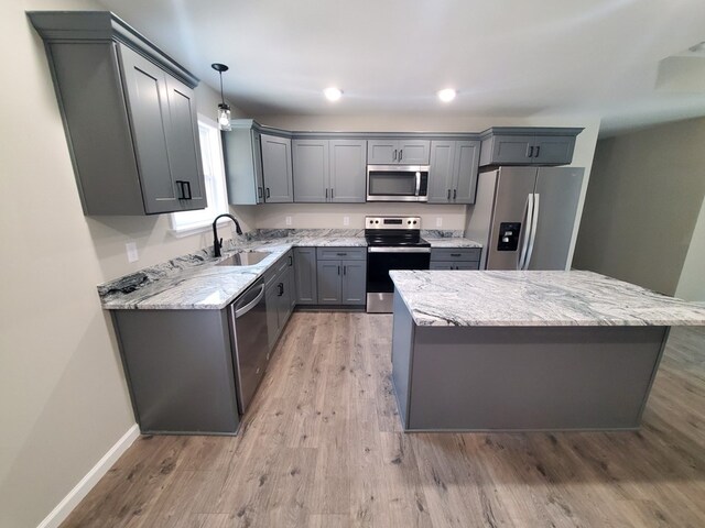 kitchen with appliances with stainless steel finishes, a center island, light stone countertops, pendant lighting, and a sink