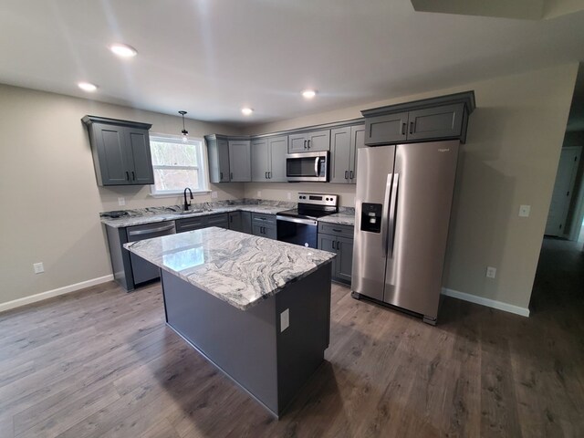 kitchen with stainless steel appliances, a sink, a center island, light stone countertops, and decorative light fixtures