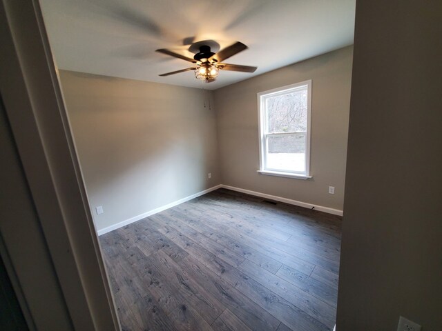 unfurnished room featuring a ceiling fan, visible vents, baseboards, and dark wood-style flooring