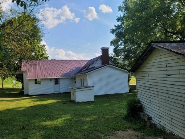 rear view of house with metal roof, a lawn, and a chimney