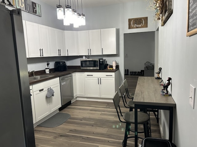 kitchen with appliances with stainless steel finishes, dark countertops, white cabinetry, and decorative light fixtures