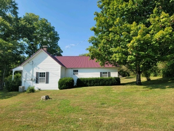 view of front facade with a front yard, metal roof, a chimney, and central air condition unit