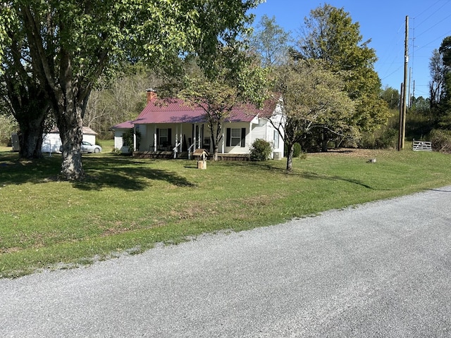 view of front facade featuring metal roof, a porch, a chimney, and a front lawn