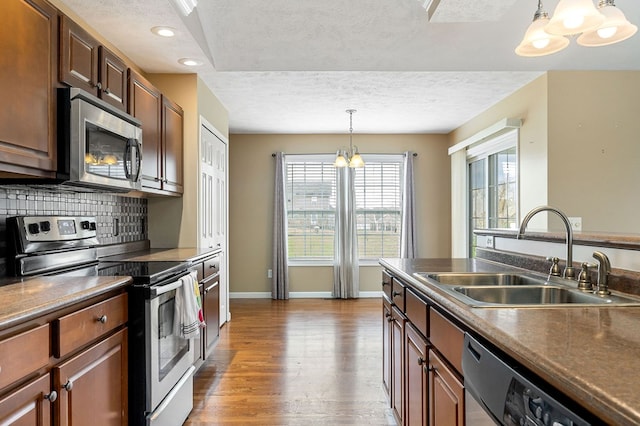 kitchen with stainless steel appliances, a sink, hanging light fixtures, tasteful backsplash, and dark countertops