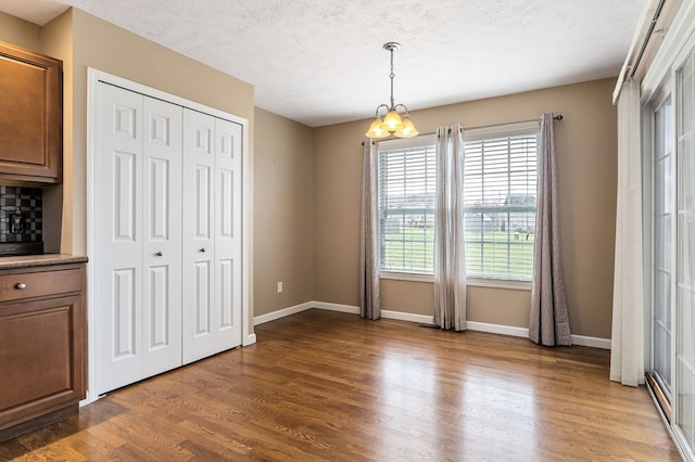 unfurnished dining area with dark wood-style floors, a textured ceiling, and baseboards