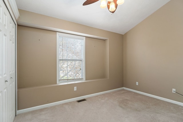 empty room with light colored carpet, a ceiling fan, baseboards, vaulted ceiling, and visible vents