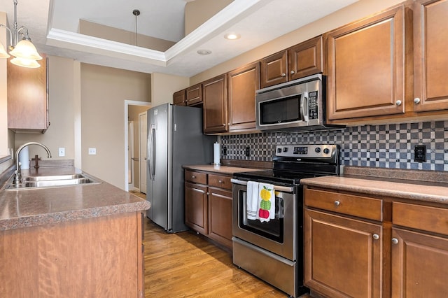 kitchen with pendant lighting, light wood finished floors, stainless steel appliances, backsplash, and a sink