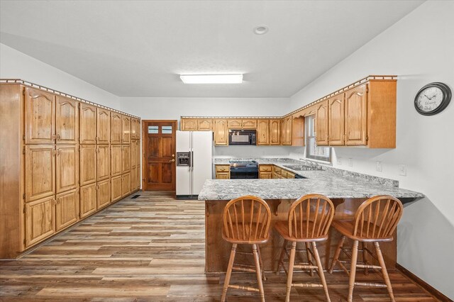 kitchen featuring a sink, white fridge with ice dispenser, range with electric cooktop, black microwave, and a peninsula