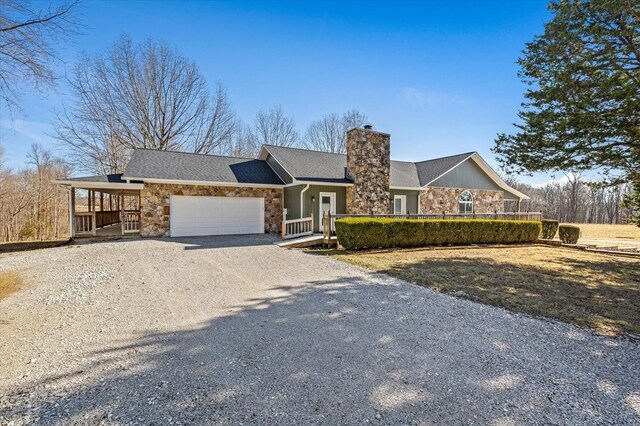 view of front facade featuring stone siding, an attached garage, a chimney, and gravel driveway