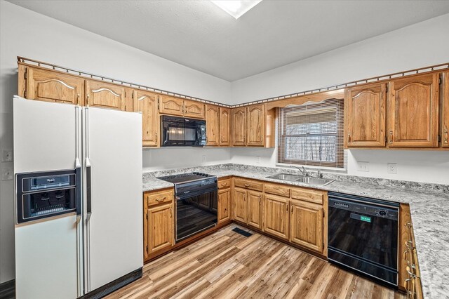 kitchen featuring black appliances, light wood-style flooring, light countertops, and a sink