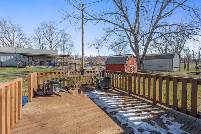 wooden terrace with a storage unit, fence, a lawn, and an outbuilding