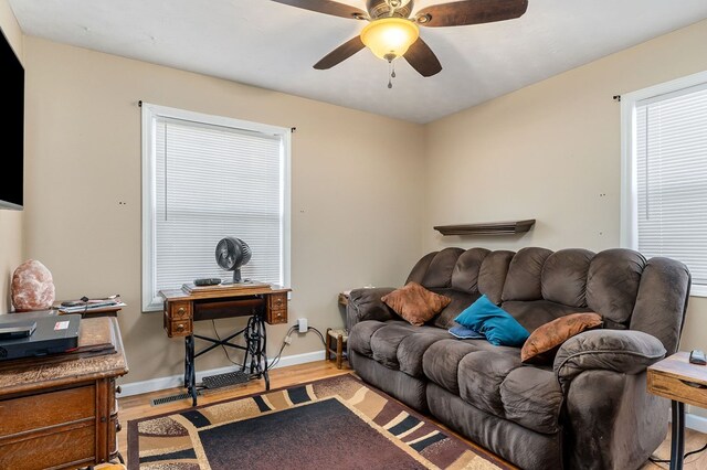 living area featuring a ceiling fan, baseboards, and light wood finished floors