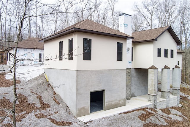 view of side of home with roof with shingles, a chimney, and stucco siding