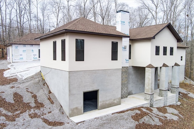 view of home's exterior with roof with shingles, a chimney, and stucco siding