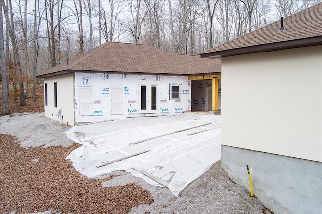 back of house with stucco siding, roof with shingles, and french doors