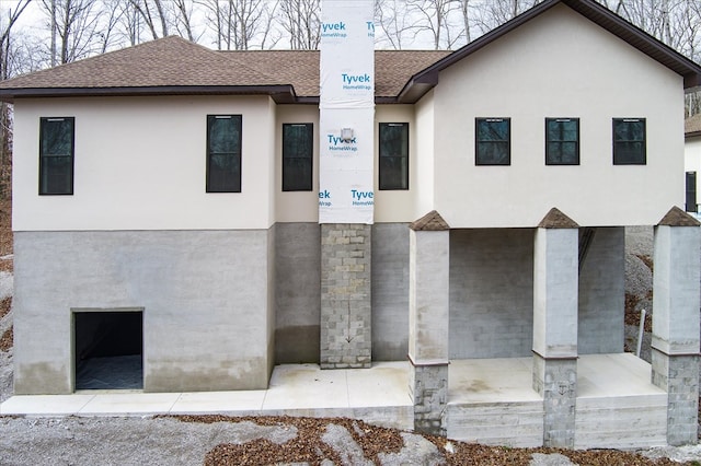 view of front facade featuring a shingled roof, a chimney, and stucco siding