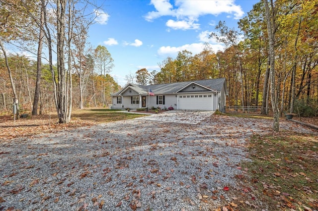 view of front of home featuring a wooded view, an attached garage, gravel driveway, and fence