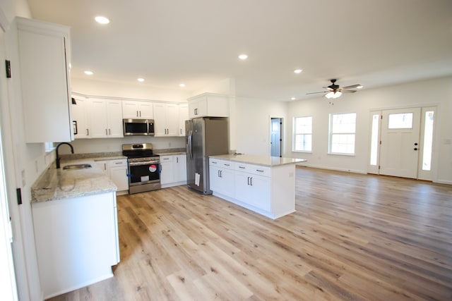 kitchen with stainless steel appliances, open floor plan, a sink, light stone countertops, and a peninsula