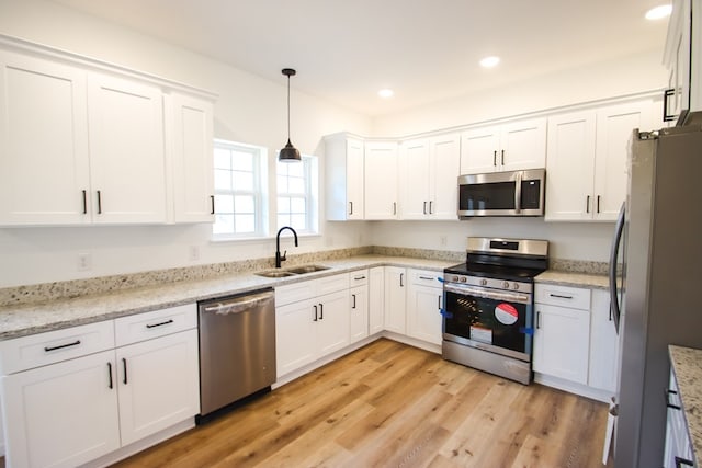 kitchen with decorative light fixtures, stainless steel appliances, white cabinetry, a sink, and light stone countertops