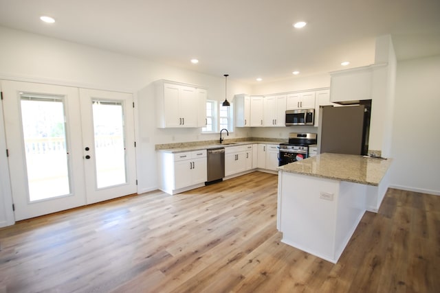 kitchen with hanging light fixtures, appliances with stainless steel finishes, white cabinets, a sink, and a peninsula