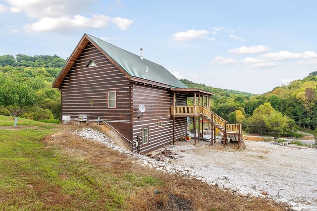 view of property exterior featuring metal roof, stairway, a wooden deck, and a view of trees