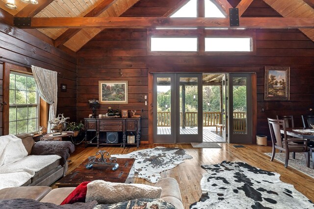 living area with wood walls, plenty of natural light, beam ceiling, and wood finished floors