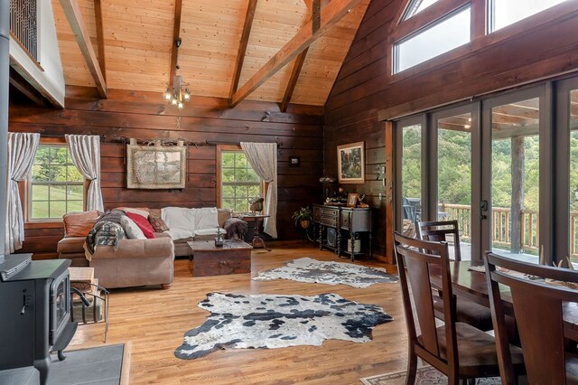 living room with light wood-style floors, a wealth of natural light, a wood stove, and beamed ceiling