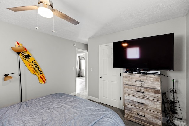 bedroom with a textured ceiling, dark colored carpet, ceiling fan, and baseboards