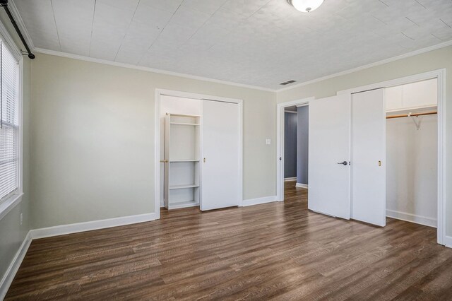 unfurnished bedroom with dark wood finished floors, two closets, visible vents, ornamental molding, and baseboards