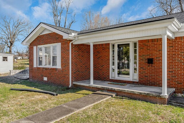 doorway to property featuring brick siding and a lawn