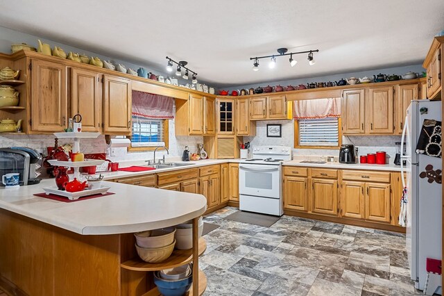 kitchen featuring a peninsula, white appliances, light countertops, and a sink