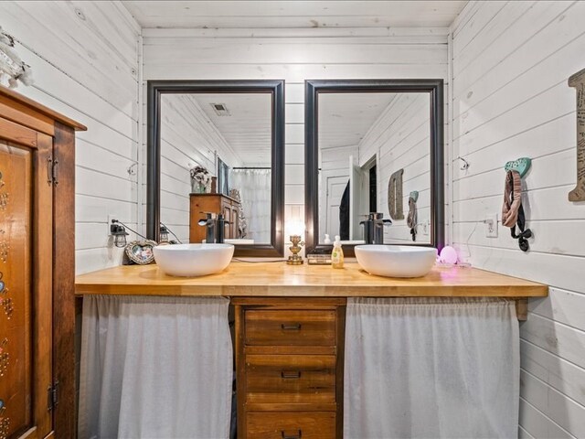 full bathroom featuring double vanity, wood walls, and a sink