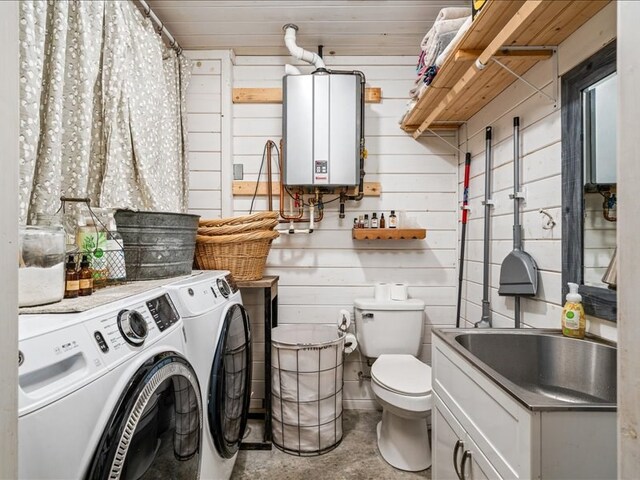 laundry room featuring tankless water heater, a sink, wooden walls, washer and dryer, and laundry area