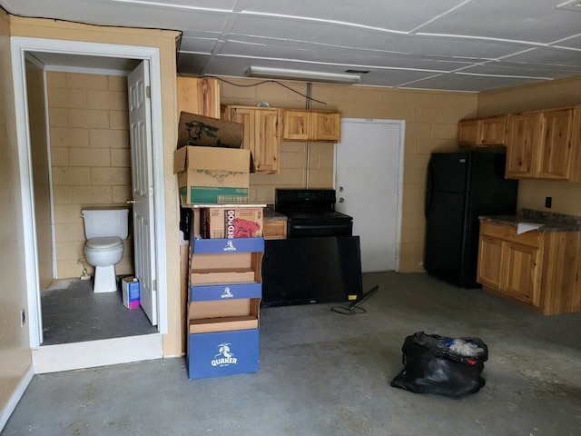 interior space with concrete block wall, black appliances, and unfinished concrete floors