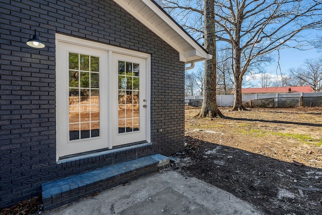 view of exterior entry featuring brick siding and fence