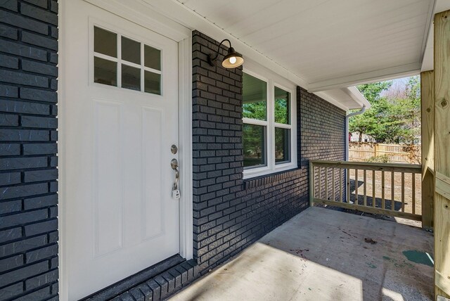 entrance to property featuring a porch, fence, and brick siding