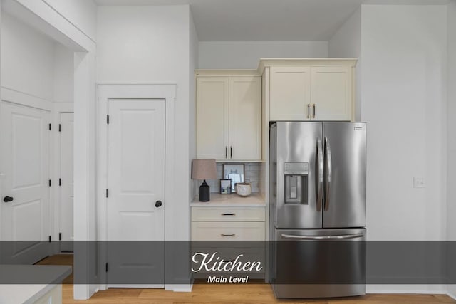 kitchen featuring tasteful backsplash, light countertops, light wood-type flooring, and stainless steel fridge