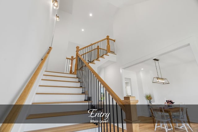 stairway with a high ceiling, wood finished floors, and recessed lighting